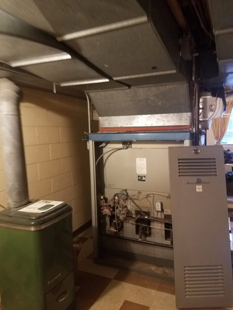 An older furnace unit with its panel removed, showing internal components during a repair or service by Shook Heating And Cooling in Livonia, MI.