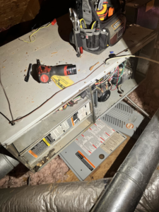 An HVAC furnace unit being serviced with tools in an attic by Affordable heating and air conditioning in Meridian, MS.