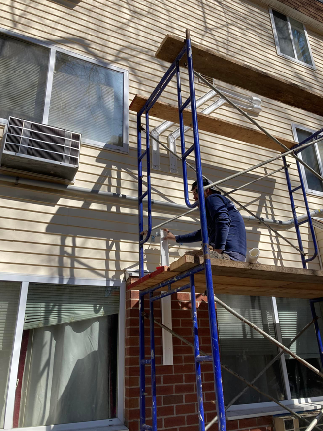 A worker on scaffolding performing HVAC installation or repair on a building exterior for Express Plumbing in Hatfield, MA.
