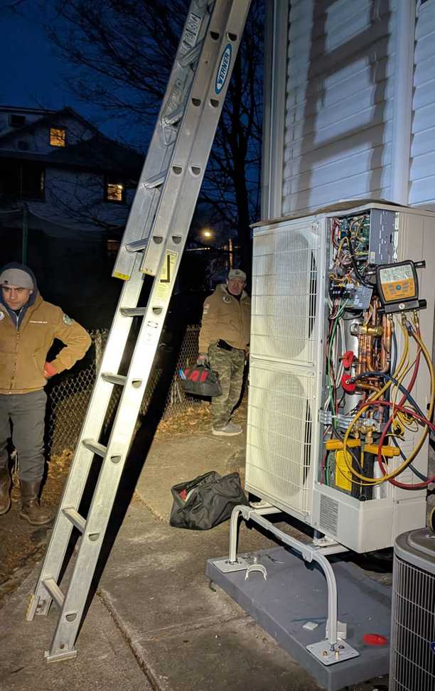 HVAC technicians installing or servicing an outdoor unit with gauges connected for Frontier 44 Corp. in Melrose, MA.