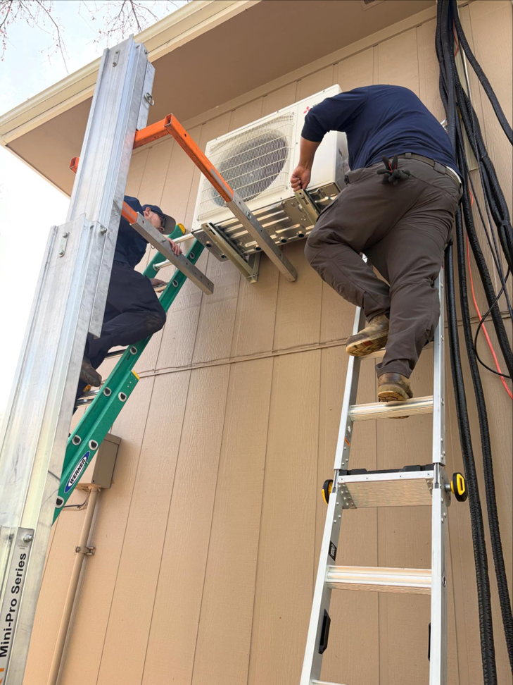 HVAC installers mounting an outdoor condenser unit on a building with ladders and a lift for Royal Heating & Air LLC in Sparks, NV