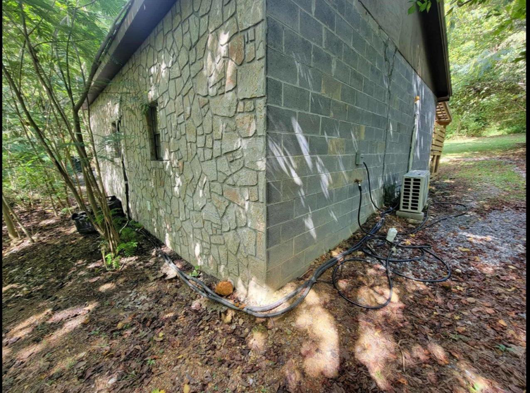 An HVAC mini-split condenser unit installed on a cinder block wall at a building corner by Smoky Mountain Ducts & Vents in New Market, TN.