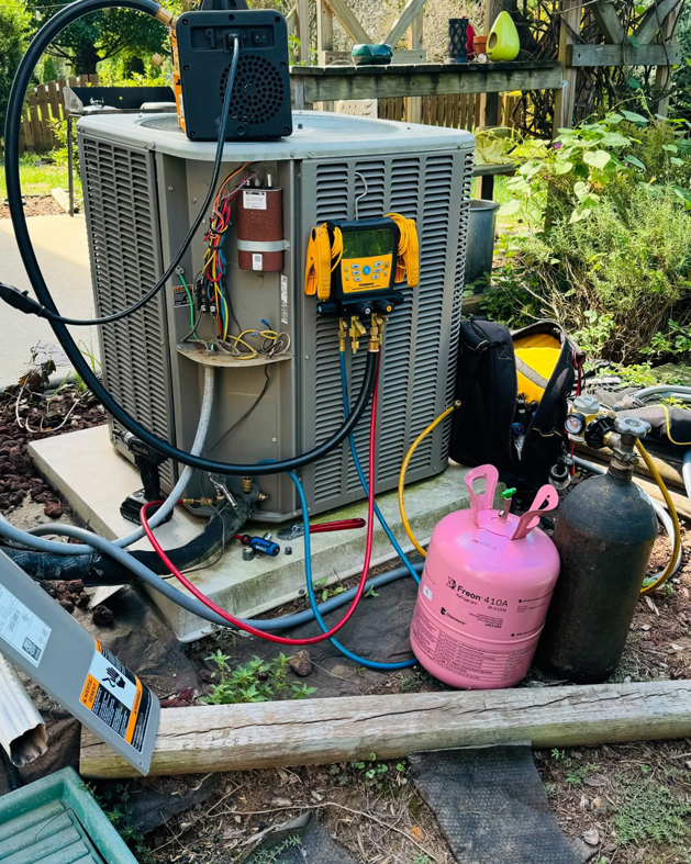 An outdoor HVAC condenser unit being serviced with refrigerant gauges and a Freon R410A tank by Ortez Home Services LLC in Charlotte, NC.