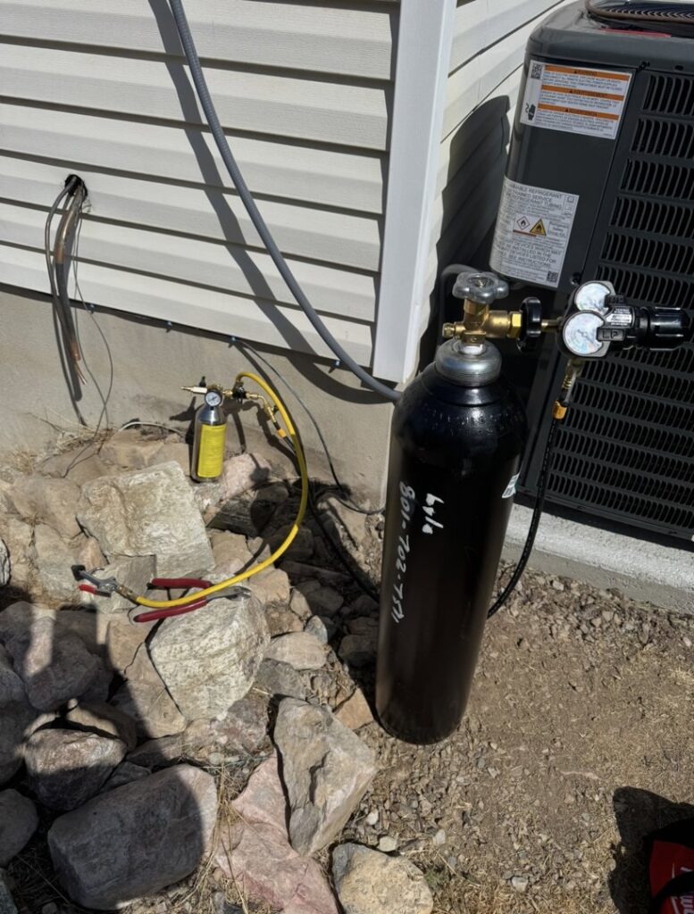 A refrigerant tank and gauges connected to an outdoor HVAC unit by LeoAir, LLC in West Jordan, UT.