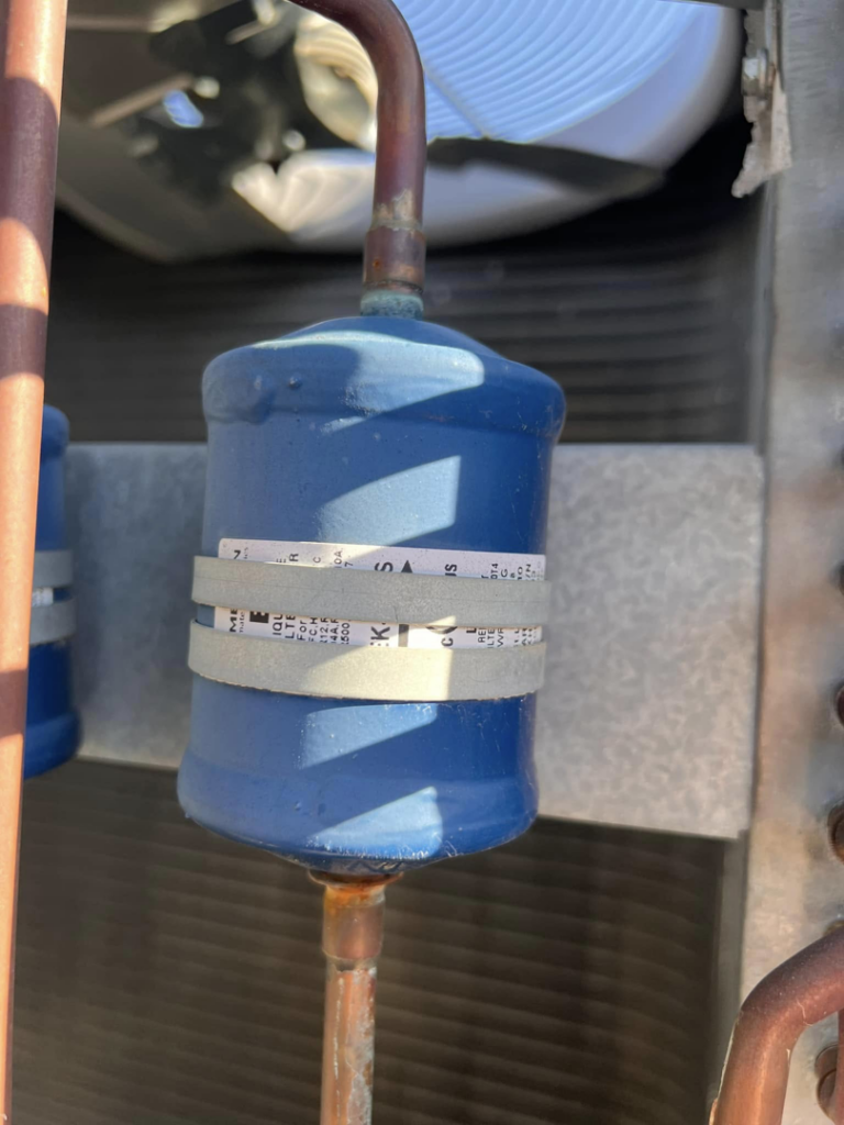 A blue refrigerant filter dryer connected to copper lines within an HVAC unit by Mead Heating and Cooling in Kansas City, MO.
