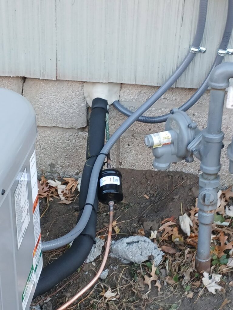 Close-up of outdoor HVAC refrigerant and gas lines with a filter/dryer, installed by A-1 HVAC in Kansas City, KS.