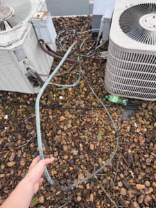 A technician inspecting or repairing a copper refrigerant line near outdoor HVAC units by AirWorx - Heating & Cooling in Midvale, UT.