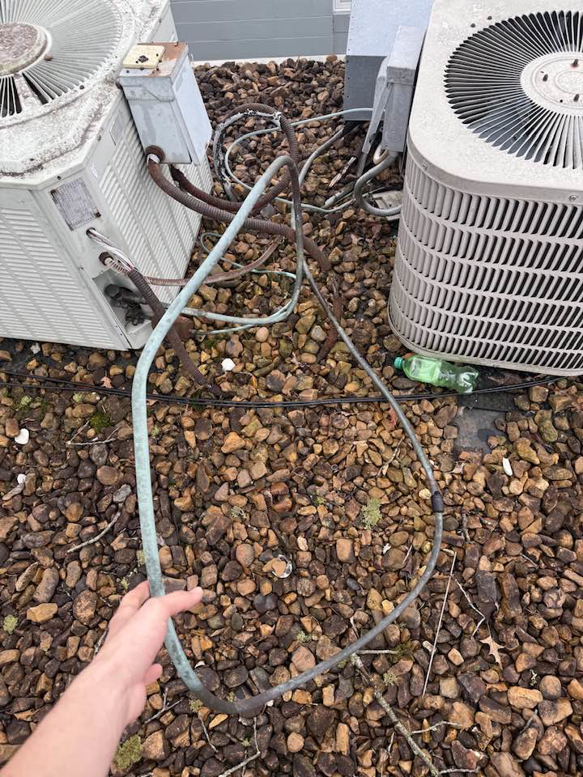 A technician inspecting or repairing a copper refrigerant line near outdoor HVAC units by AirWorx - Heating & Cooling in Midvale, UT.