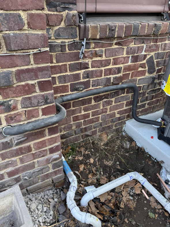 HVAC refrigerant lines and condensate drain piping installed along a brick wall by Indoor Weather Solutions LLC in Broken Arrow, OK.