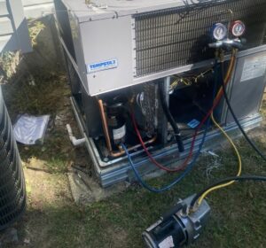 An outdoor AC unit undergoing refrigerant service with gauges and a vacuum pump by Triune Air in Smithville, TN.