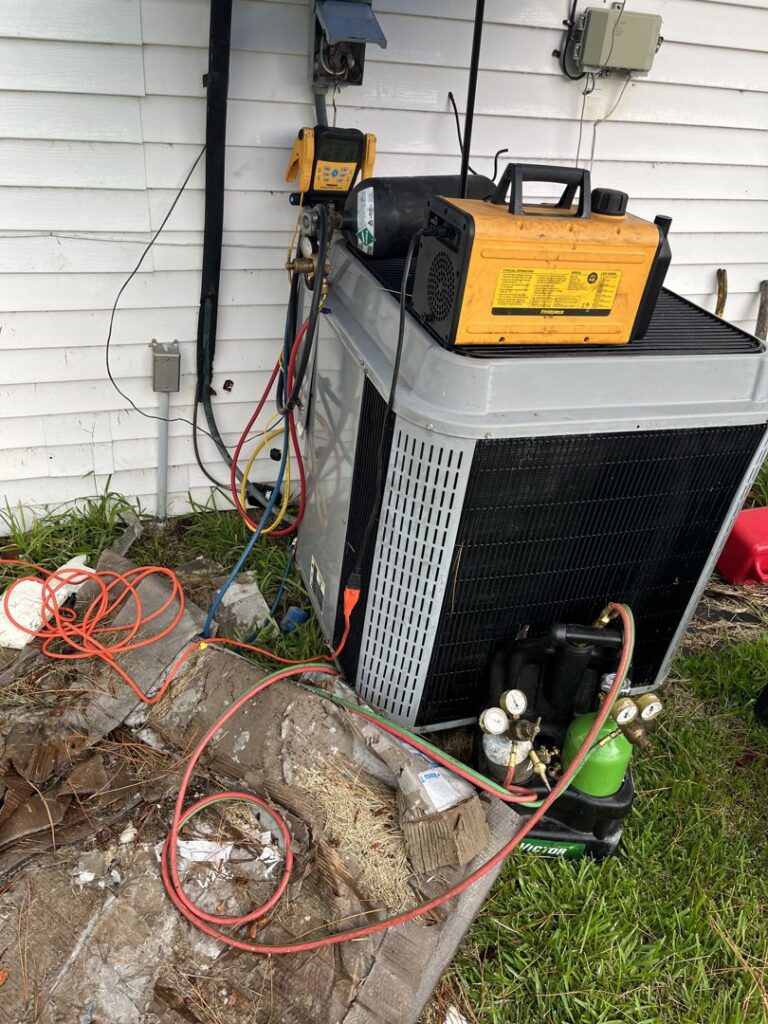 An HVAC technician performing refrigerant service on an outdoor condenser unit with gauges and hoses at Keith HVAC & Electrical Enterprises LLC in New Orleans, LA.