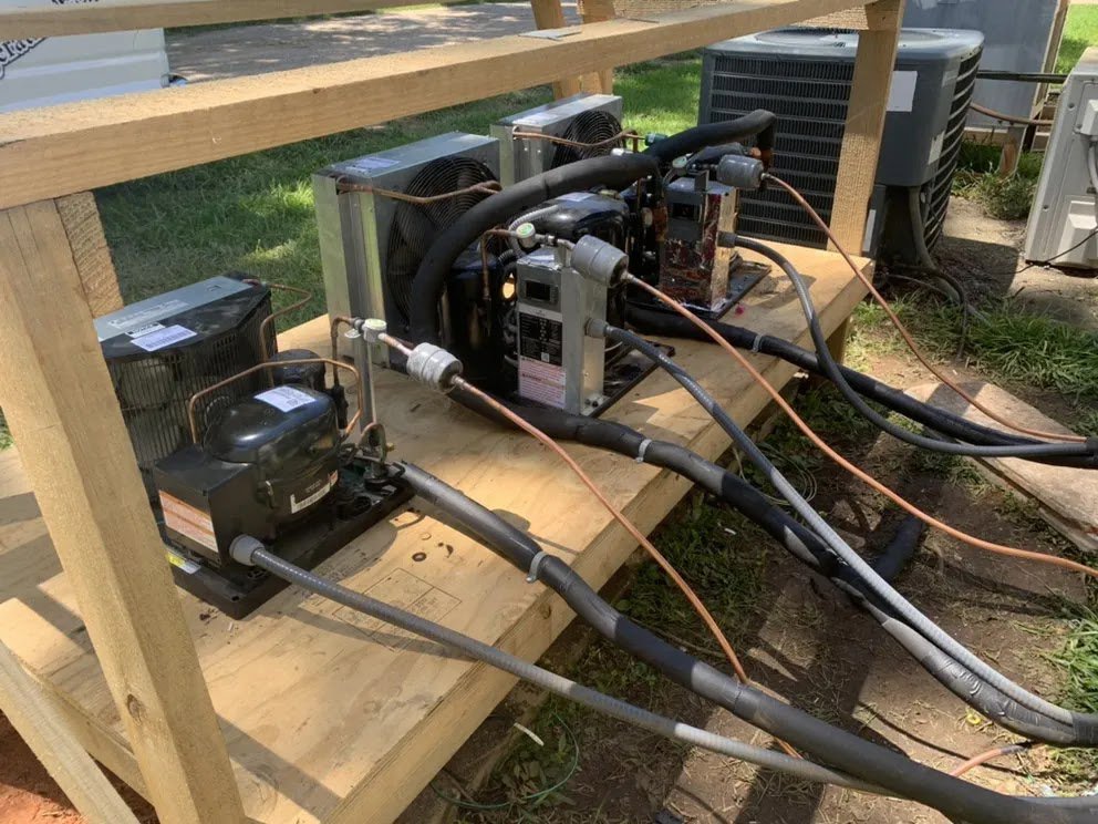 A setup of multiple HVAC refrigeration compressors and coils on a wooden frame, demonstrating technical work by Netherland Air Conditioning LLC in Mobile, AL.