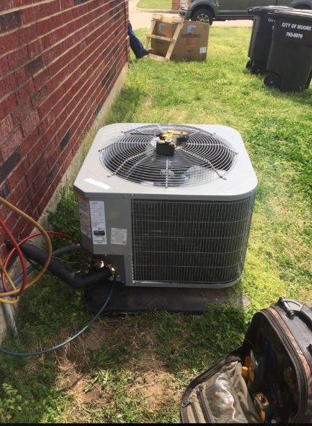 An outdoor AC unit undergoing repair service with gauges and tools, performed by Rhino Heating and Air Conditioning LLC in Norman, OK.