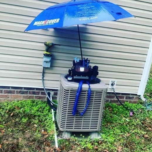 An outdoor air conditioning unit undergoing repair with tools and an umbrella for shade by Climate Mechanical in Dinwiddie, VA.