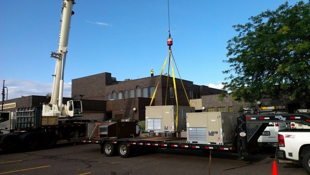 Crane lifting multiple commercial HVAC rooftop units from a trailer for installation by Benck Mechanical Inc in Somerset, WI.