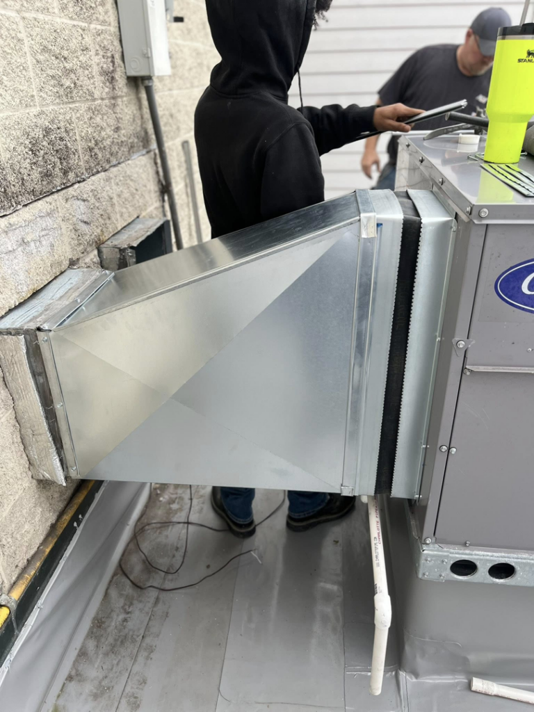 A technician installing a rooftop HVAC unit and ductwork for WV Heating and Air in Morgantown, WV