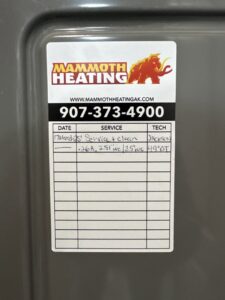 A service record sticker from Mammoth Heating on an HVAC unit, detailing a recent service and cleaning in Wasilla, AK.