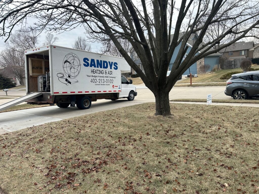 A Sandys Heating & Air service truck with a ramp at a residential job site in Papillion, NE.