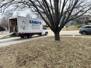 A Sandys Heating & Air service truck with a ramp at a residential job site in Papillion, NE.