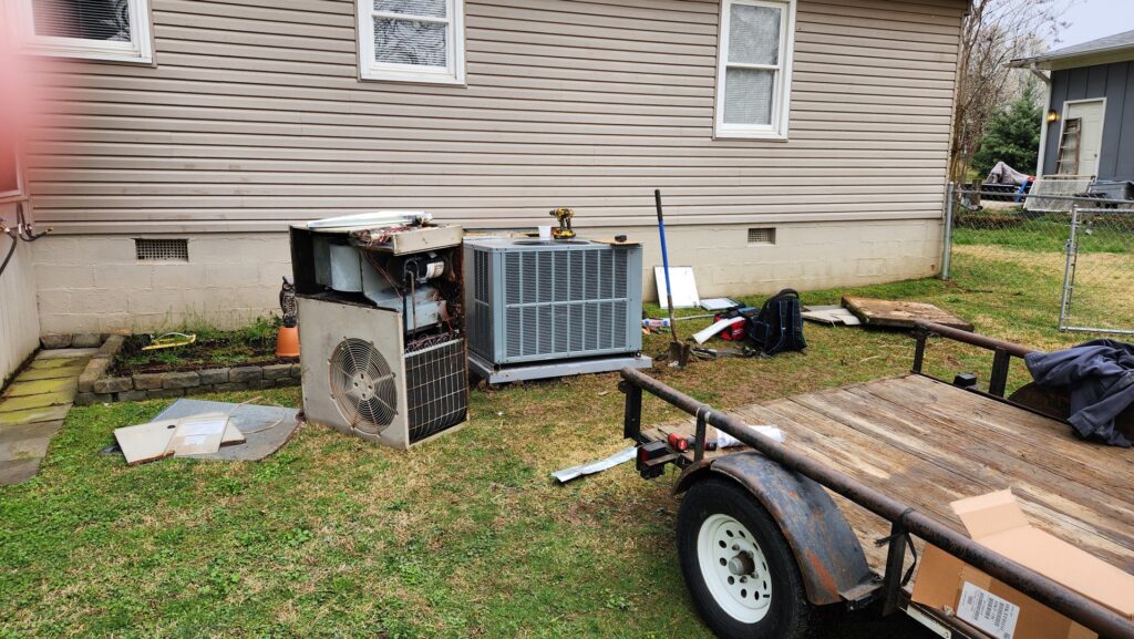 Old HVAC units being removed during a system replacement, with a new condenser unit installed in the background by Bama Air Systems in Cullman, AL.