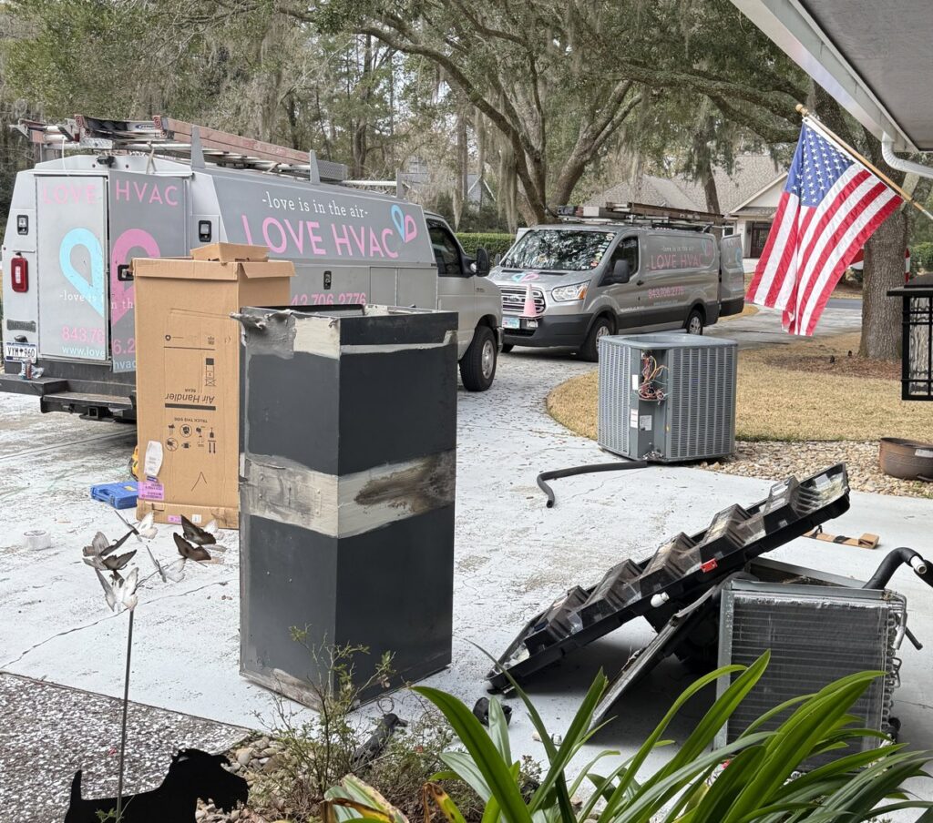 Love HVAC LLC vans parked at a residence during an HVAC system replacement, with old units and new equipment visible in Bluffton, SC.