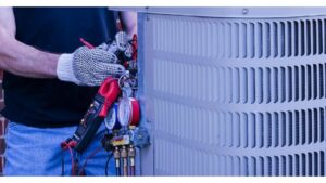 An HVAC technician performing a repair on an outdoor air conditioning unit with gauges and tools for Primary Air Home Services in Aurora, CO.