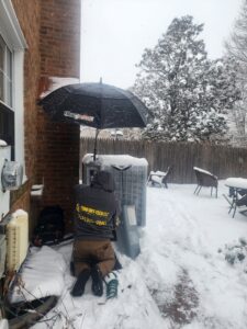 A Comfort-Tech llc technician servicing an outdoor AC unit in the snow in Alexandria, VA.
