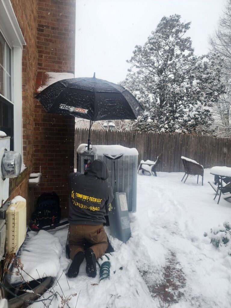 A Comfort-Tech llc technician servicing an outdoor AC unit in the snow in Alexandria, VA.