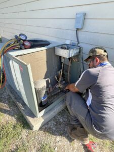 An HVAC technician performing repair or maintenance on an outdoor AC unit with gauges connected for South Texas Climate Control in San Antonio, TX
