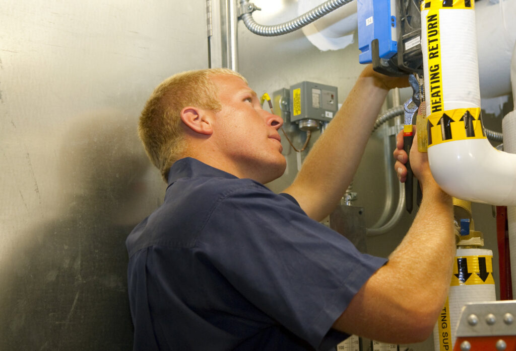 An HVAC technician adjusting pipes and controls in an indoor mechanical room for Climate Systems, Inc. in Sioux Falls, SD.