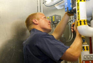 An HVAC technician adjusting pipes and controls in an indoor mechanical room for Climate Systems, Inc. in Sioux Falls, SD.