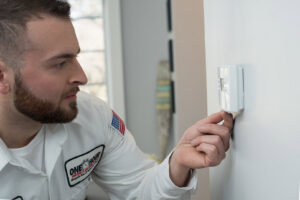 An HVAC technician adjusting a thermostat during a service call for One Hour Heating & Air Conditioning of Albany in Albany, NY