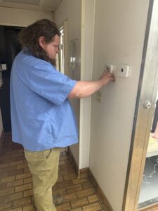 An HVAC technician adjusting multiple thermostats on a wall for Direct Service HVAC & Maintenance in Lewisburg, OH.