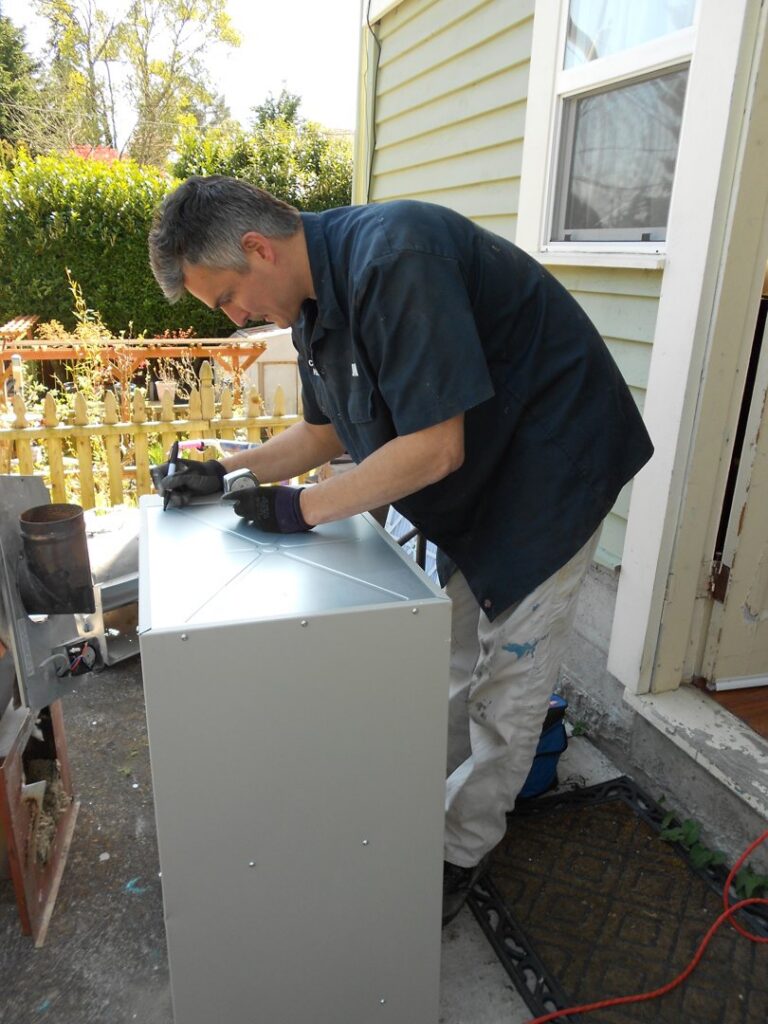 An HVAC technician from Columbia Heating & Air Conditioning assembling metal ductwork components outdoors in Kent, WA.