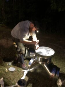 An HVAC technician assembling metal ductwork components outdoors at night for Workman Mechanical in Graham, NC.