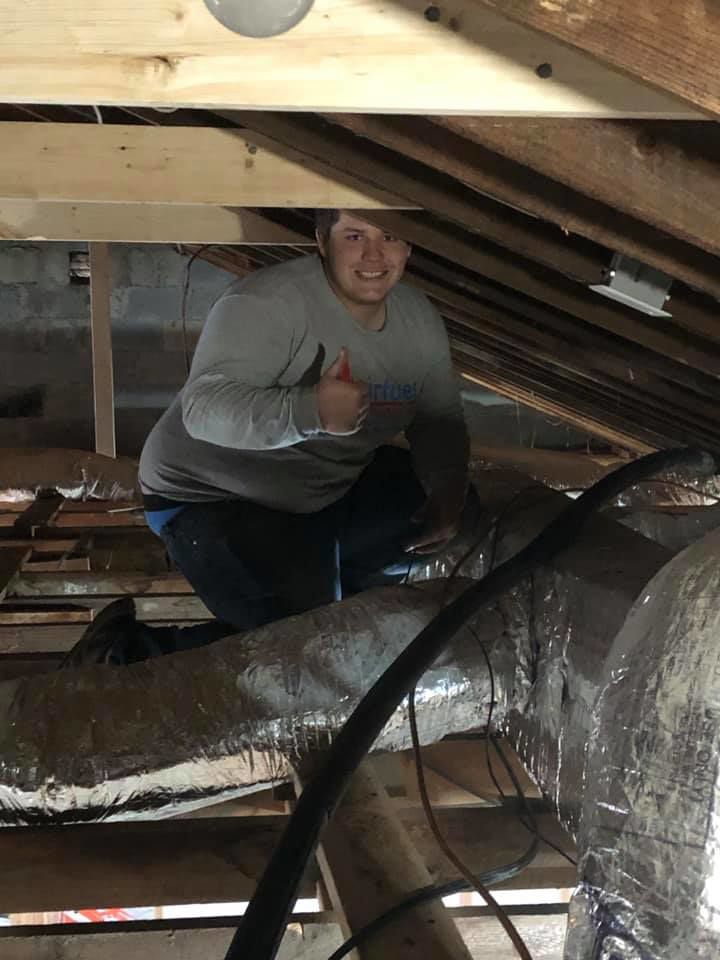 An HVAC technician inspecting or installing ductwork in an attic for Virtues Mechanical LLC in Baltimore, MD.