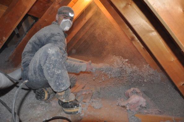 An HVAC technician blowing insulation into an attic for Assured Energy Solutions in Frankfort, IL.