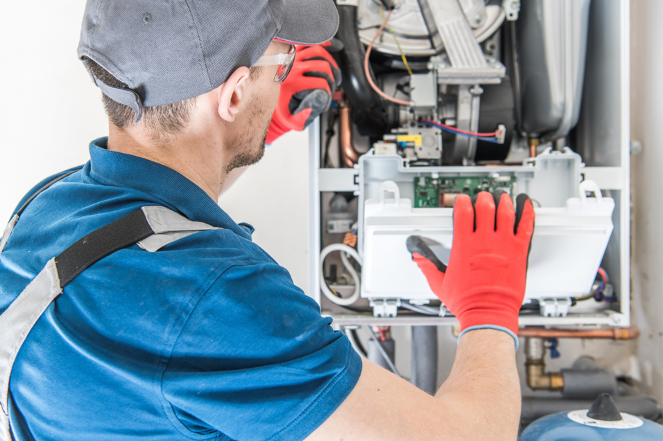 An HVAC technician performing maintenance or repair on a boiler system for Basic HVAC in Indianapolis, IN.