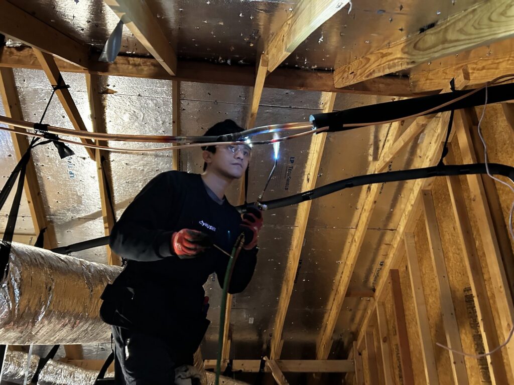 HVAC technician brazing copper refrigerant lines in an attic during installation for Benavidez Heating & Air Conditioning In, Arlington, TX.