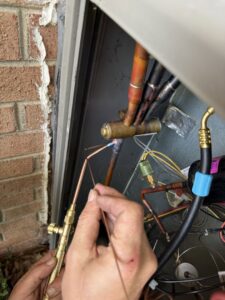 An HVAC technician brazing copper refrigerant lines on an outdoor air conditioning unit for Know A Guy Heating & Air Conditioning in Kernersville, NC.