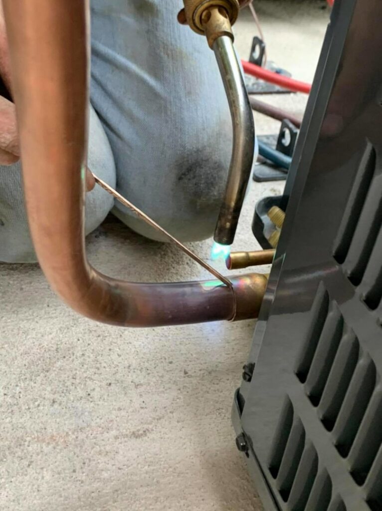 An HVAC technician brazing copper pipes for an air conditioning unit by Detroit Metro Mechanical, Inc. in Harrison Township, MI.