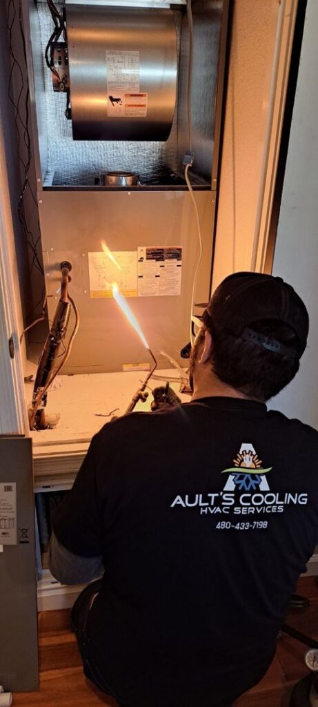 An HVAC technician from Ault's Cooling HVAC Services LLC brazing components on an indoor furnace unit in Chandler, AZ.