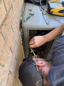 An HVAC technician brazing refrigerant lines on an outdoor unit during a service call by Know A Guy Heating & Air Conditioning in Kernersville, NC.