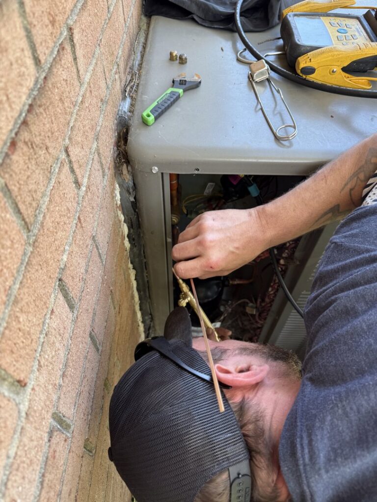 An HVAC technician brazing refrigerant lines on an outdoor unit during a service call by Know A Guy Heating & Air Conditioning in Kernersville, NC.