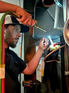 An HVAC technician brazing copper refrigerant lines during an installation or repair by Stoker Mechanical Heating & Air Conditioning in Lawrence, KS.