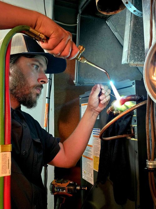 An HVAC technician brazing copper refrigerant lines during an installation or repair by Stoker Mechanical Heating & Air Conditioning in Lawrence, KS.