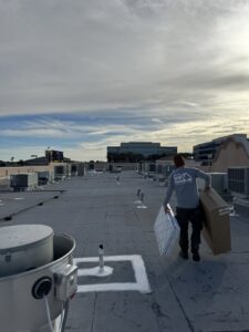 An HVAC technician carrying new air filters across a commercial rooftop for Rogue Mechanical in Las Vegas, NV.