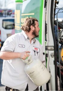 An HVAC technician from DFH Company Heating and Air Conditioning carrying a refrigerant tank from a service van in Louisville, KY
