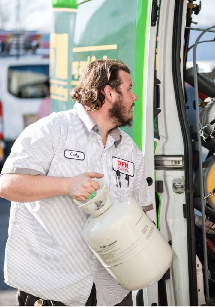 An HVAC technician from DFH Company Heating and Air Conditioning carrying a refrigerant tank from a service van in Louisville, KY