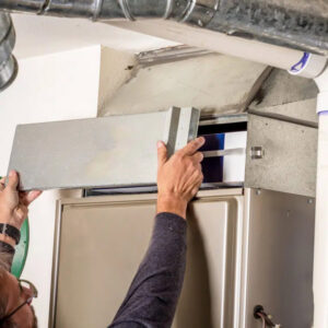 An HVAC technician changing an air filter in a furnace or air handler for Absolute Plumbing, Electrical, Heating & Air in Denver, CO